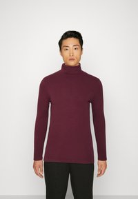 Jersey de cuello alto burdeos en un diseño ajustado con mangas largas, hecho de una tela lisa y elástica. Combinado con pantalones negros.