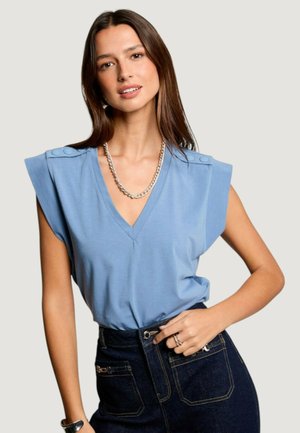 Haut bleu clair en v avec des boutons à l'épaule, à manches courtes, et texture douce. Assorti à une jupe en denim foncé avec des poches avant.