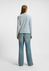 Helles blaues Langarmoberteil kombiniert mit weit geschnittenen, verwaschenen Jeans, die über hintere Taschen und einen lässigen Schnitt verfügen. Der glatte Stofftextur ist sichtbar.