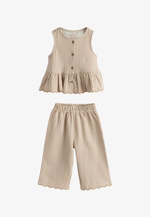 Top bej cu dungi albe, fără mâneci, cu nasturi și tiv cu volane, asortat cu pantaloni scurți cu talie elastică și margini dantelurate.