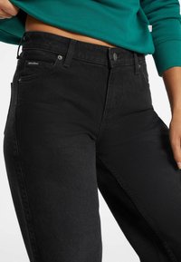Jeans in denim neri con vestibilità slim, tessuto resistente, tasche frontali, chiusura con bottone e dettagli di cucitura sottili.