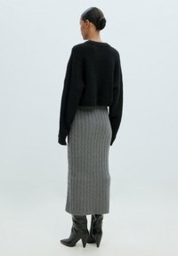 Schwarzer, grob gestrickter, cropped Pullover kombiniert mit einem eng sitzenden, texturierten, grauen Rippstrickrock und schwarzen spitzen, hohen Stiefeln. Rückansicht.