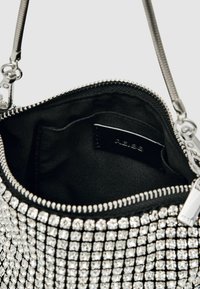Črna torbica z teksturiranim zunanjim delom okrašena s srebrnimi kamni, z zadrgo in gladkim tekstilnim notranjim delom.