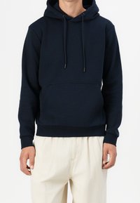 Mörkblå hoodie gjord av mjukt tyg med en framficka, justerbara snören och ribbade ärmslut och nederkant. Bärs med ljusa byxor.