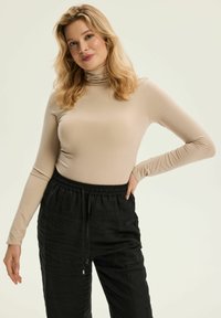 Beige Langarm-Turtleneck-Oberteil, kombiniert mit schwarzen Jogginghosen mit Kordelzug; glattes Material und lässige Passform mit subtiler Textur und Details.