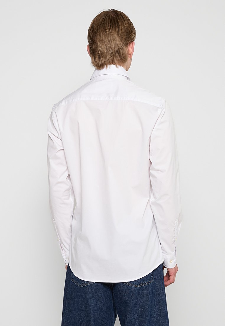 Camicia bianca a maniche lunghe realizzata in tessuto liscio, con colletto classico e polsini abbottonati, orlo dritto e dettagli sulla spalla sul retro.
