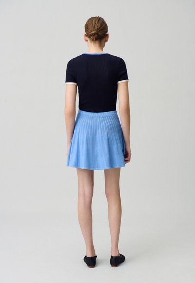 Top negro de manga corta con textura acanalada y detalles blancos, combinado con una falda plisada de color azul claro, con una cinturilla y un dobladillo por encima de la rodilla.
