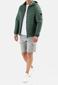 Green quilted jacket with a hood, gray cargo shorts, and white sneakers. Features a zippered front and textured fabric details.