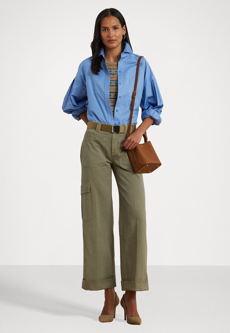 Camisa de botones azul claro, pantalones cargo beige con puños enrollados, cinturón a juego, bolso de mano marrón claro y tacones beige. Detalle de punto texturizado en la camisa.