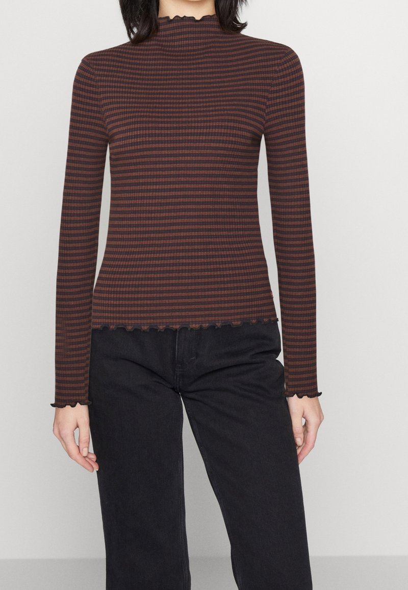 Långärmad, figurnära topp i mörkbrun med tunna vertikala ränder i ljusare nyanser. Har en vågig halsringning och nederkant, ribbad textur.