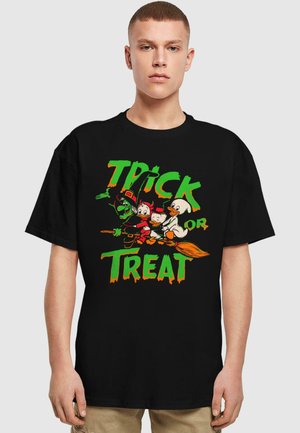 Melnā T-kreklā ir krāsains "Trick or Treat" dizains ar multfilmu varoņiem, kas lido uz slotas. Spilgti zaļas, oranžas un baltas krāsas.