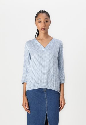 Blå mønstret bluse med V-hals og trekvartlange ermer, kombinert med et denimskjørt med en frontslitt. Myk, lettvektig stoff.