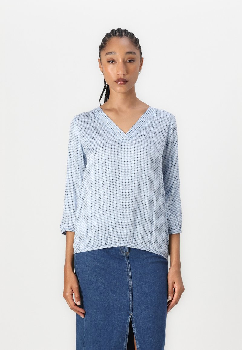 Blusa blu con motivo a V e maniche a tre quarti abbinata a una gonna di denim con uno spacco frontale. Tessuto morbido e leggero.