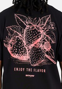 Camiseta negra con un gran gráfico rosa de fresas y hojas, con el texto "DISFRUTA DEL SABOR" debajo del diseño.