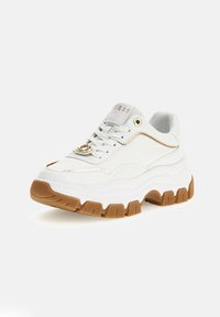 Baskets blanches avec une semelle épaisse et texturée. Présentent un logo doré et des surpiqûres dorées. Fabriquées en matériau synthétique avec une finition lisse.