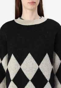 Fekete és krém színű, gyémánt mintázatú pulóver, bordázott kerek nyakkal, texturált kötött anyagból, nagyméretű fazonnal.