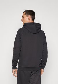 Zwarte hoodie met een gladde textuur, voorzien van een trekkoordcapuchon, raglanmouwen en gestreepte accenten langs de zijkanten, gestyled met bijpassende broek.