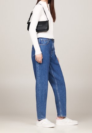 Lichtgewicht wit geribd topje gecombineerd met losse blauwe jeans, gedragen met witte sneakers. Een kleine zwarte handtas hangt over de schouder.