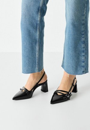 Zwarte gepatineerde leren slingback hakken met een spitse neus en blokhak. Kruisende banden met gespaccenten. Gecombineerd met blauwe denim.
