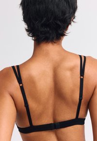 Schwarzer BH mit verstellbaren dünnen Trägern, hergestellt aus glattem Stoff. Verfügt über einen Haken- und Ösenverschluss auf der Rückseite. Minimalistisches Design.