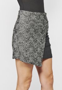 Jupe en motif chevrons noir et blanc avec un ourlet asymétrique, un tissu texturé, une taille haute et un design décontracté.