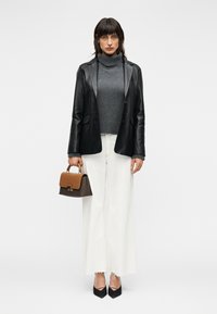 Μαύρο δερμάτινο σακάκι πάνω από γκρι μπλουζάκι με ψηλό λαιμό, συνδυασμένο με φαρδιά λευκά παντελόνια, μαύρες μυτερές γόβες και μικρή καφέ τσάντα χειρός με επάνω λαβή.