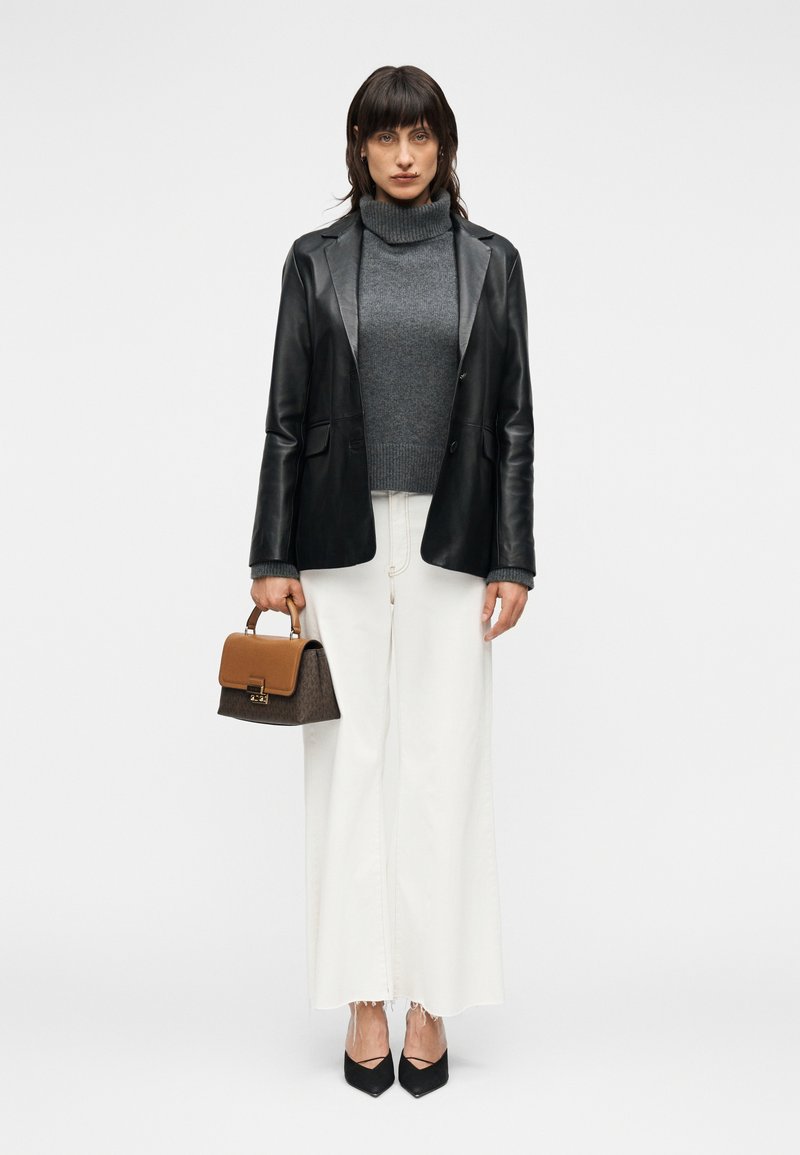 Μαύρο δερμάτινο σακάκι πάνω από γκρι μπλουζάκι με ψηλό λαιμό, συνδυασμένο με φαρδιά λευκά παντελόνια, μαύρες μυτερές γόβες και μικρή καφέ τσάντα χειρός με επάνω λαβή.