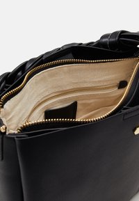 Svart läderhandväska med guldfärgad dragkedja, beige tygfoder och flätad läderhandtag.