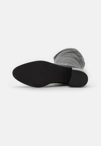 Bota de tela gris hasta la rodilla con una textura suave, que cuenta con una suela de goma negra y un ligero tacón; diseñada con un aspecto arrugado y holgado.