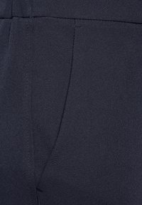 Marinblått tyg, slät textur, har en sidoficka med fina sömnadsdetaljer och en skräddarsydd passform, lämplig för formell eller professionell klädsel.