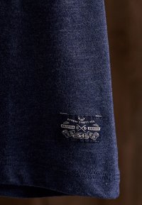 Tmavě modrá tkanina s jemnou texturou má na lemu tkanou štítku s nápisem "Regent Street" a "Britský design."