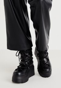 Zapatillas de plataforma negras hechas de cuero suave, con suelas gruesas, detalles de cordones intrincados y un diseño de caña alta.