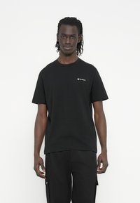 Juodas medvilninis marškinėlis trumpomis rankovėmis ir apvalia iškirpte. Kairėje krūtinės pusėje mažas baltas logotipas. Paprastas dizainas, be raštų.