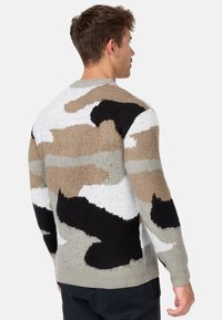 Striktrøje med camouflage mønster i beige, sort, hvid og grå. Tekstureret garn med kontrastfarver på ryggen.