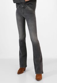 Flared gray jeans made of denim, featuring a mid-rise waist, classic five-pocket design, and subtle fading. Complemented with brown heeled boots.
