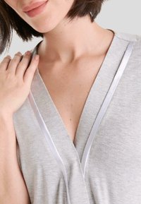 Prenda gris con un escote en V profundo, acentuada con un ribete de satén blanco. Tejido suave y texturizado con un corte relajado.