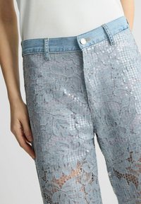 Pantaloni in denim azzurro chiaro con sovrapposizione di pizzo floreale, decorati con paillettes, dotati di una vita standard e una forma aderente.