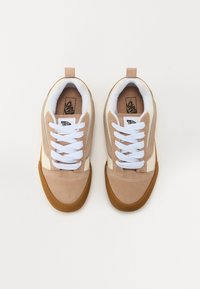 Tenisi bej și crem cu partea superioară din suede, șireturi albe, talpă din cauciuc de tip gumă și branding pe limbă. Au un design cu profil scăzut.