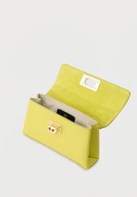 Κίτρινη υφασμάτινη τσάντα χειρός με κούμπωμα σε χρυσό τόνο, ανοιχτή για να αποκαλύψει μπεζ εσωτερικό και μια μαύρη κάρτα στην εσωτερική θήκη σε λευκό φόντο.