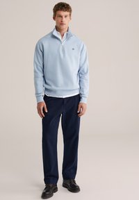 Šviesiai mėlynas užsegamas džemperis iš minkštos medžiagos, po juo baltas marškinėliais su apykakle ir tamsiai mėlynos kelnės. Juodi batai papildys šią aprangą.