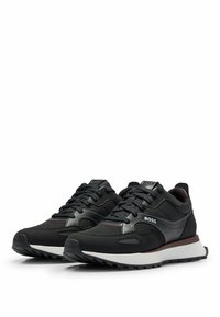 Schwarze Sport Sneakers aus einer Kombination aus glatten und strukturierten Materialien, mit einer weißen Zwischensohle und dezenten roten Akzenten. Schnürdesign.
