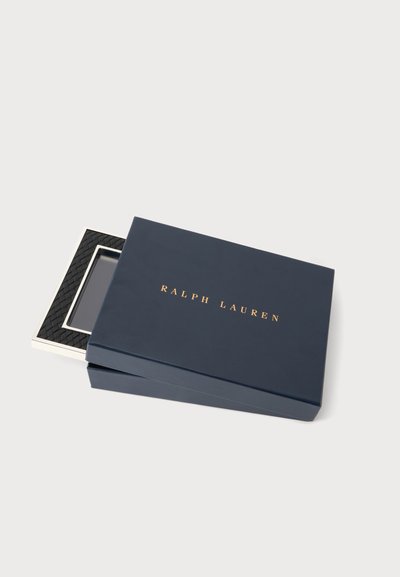 Το κουτί Ralph Lauren σε ναυτικό μπλε χρώμα ανοίγει για να αποκαλύψει μια υφαντή μαύρη και ασημένια ορθογώνια αγκράφα ζώνης μέσα.