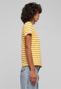 Gul- og hvidstribet t-shirt med korte ærmer, rund halsudskæring og en afslappet pasform, parret med lyseblå denimjeans.