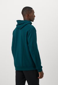Teal hoodie with a large, adjustable hood, long sleeves, and ribbed hem, made of soft, textured fabric. Smooth back design with no graphics.