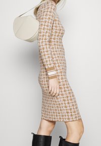 Robe en maille marron à motifs avec manches longues, associée à un sac bandoulière crème et des bottes noires hautes jusqu'au genou. Design simple et coupe ajustée.