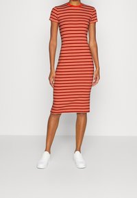 Czerwono-biała sukienka bodycon w paski z krótkimi rękawami i okrągłym dekoltem, wykonana z miękkiego, elastycznego materiału. W połączeniu z białymi trampkami.