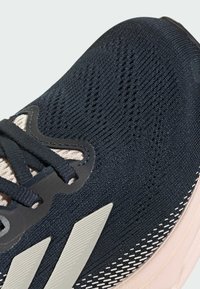 Scarpa da ginnastica blu navy con upper in mesh testurizzato, accenti neri e suola rosa chiaro. Presenta sovrapposizioni sintetiche a righe e lacci.