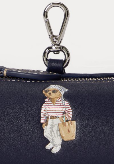 Navy leather pouch with silver clip and a bear wearing sunglasses, striped shirt, white pants, headscarf, and holding a tan tote bag.