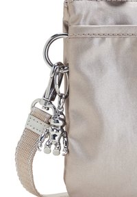 Ljusbeige axelväska med en glansig yta, med en klämma i silverfärgad metall och en metallisk berlock fäst vid en vävd rem.