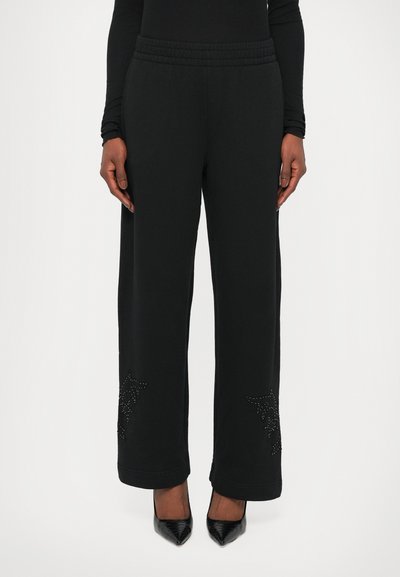 Pantalons de survêtement noirs avec une taille élastique, coupe large et motif étoile décoratif en strass sur les côtés inférieurs. Texture de tissu lisse.